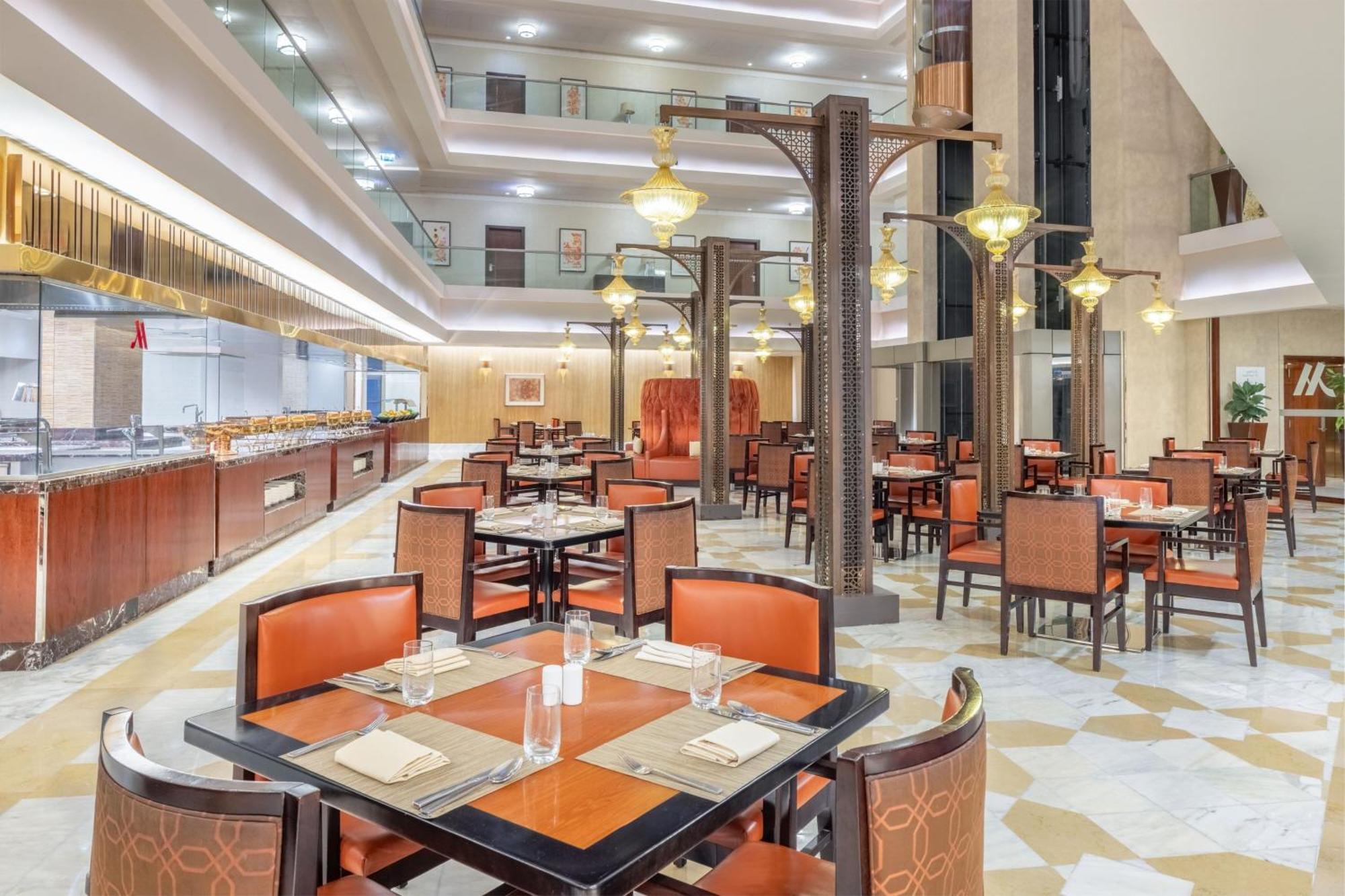 Jabal Omar Marriott Hotel Makkah Mecca Exterior photo The photo depicts an elegant dining area within a restaurant. The space features several tables, each set with plates, glasses, and napkins. The seating consists of brown chairs with orange accents. The restaurant has a modern design, highlighted by 