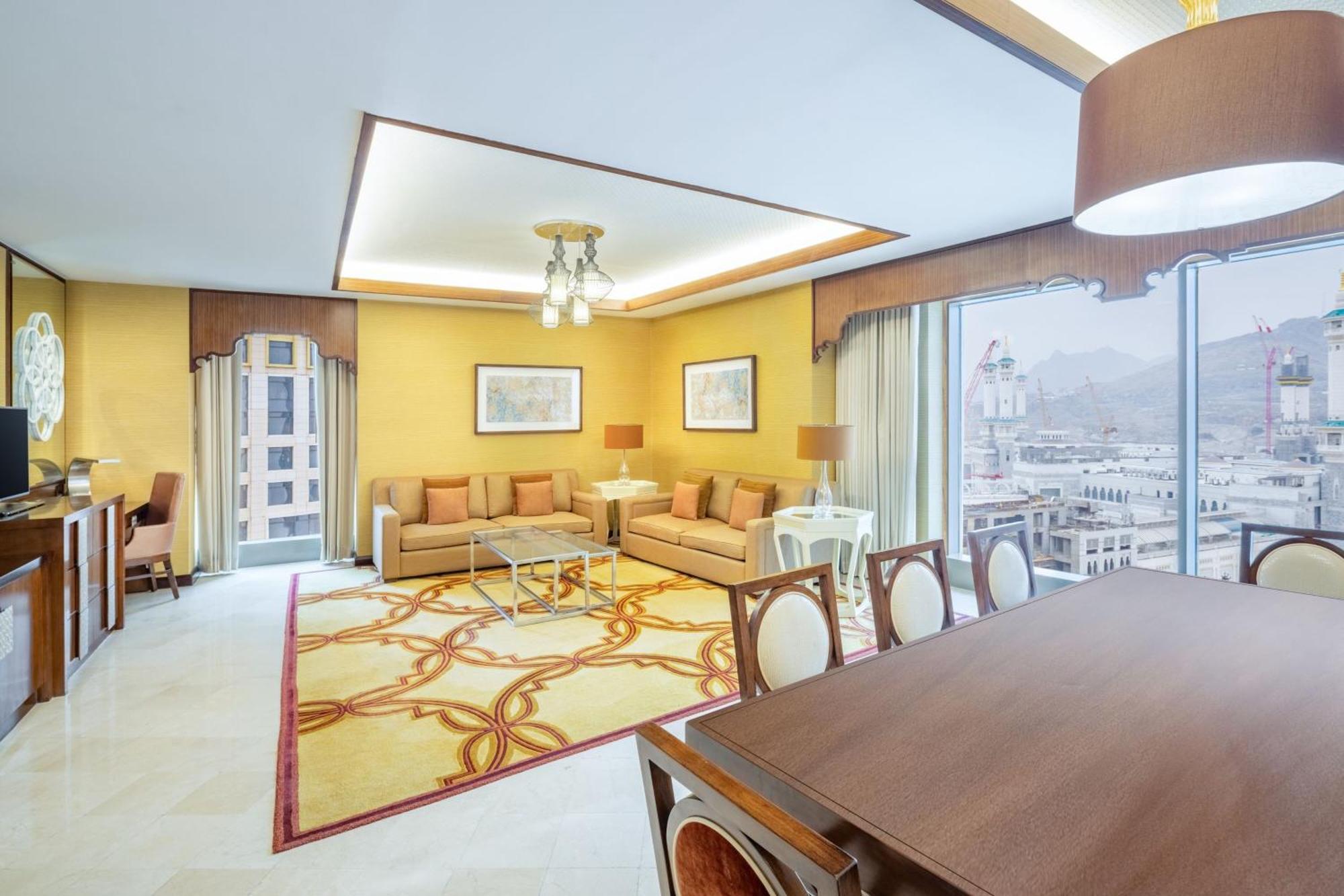 Jabal Omar Marriott Hotel Makkah Mecca Exterior photo The photo shows a spacious and elegantly designed living area. The walls are painted in a warm yellow shade, complemented by large windows that provide plenty of natural light and a view of the outside. 

In the center, there's a seating area with a 