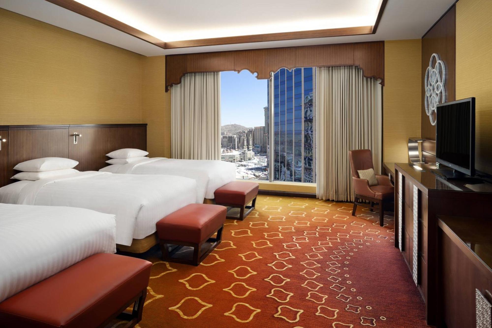 Jabal Omar Marriott Hotel Makkah Mecca Exterior photo The photo shows a hotel room with a modern and inviting design. It features two beds with white bed linens, positioned next to a large window that offers a view of the outside. The room is decorated with warm colors, including a patterned carpet in s